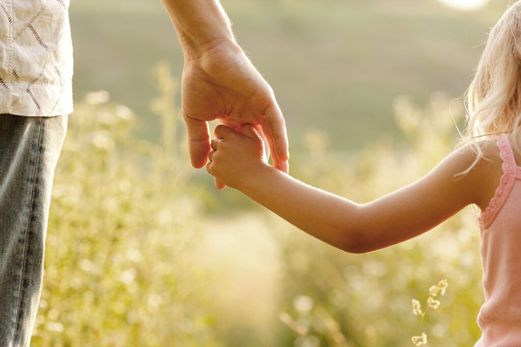 A parent holding a child’s hand outdoors